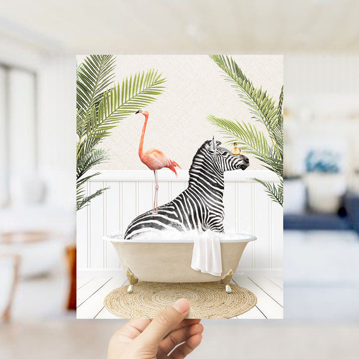A hand holds up a framed image depicting a zebra sitting in a bathtub, with a pink flamingo standing on its back.