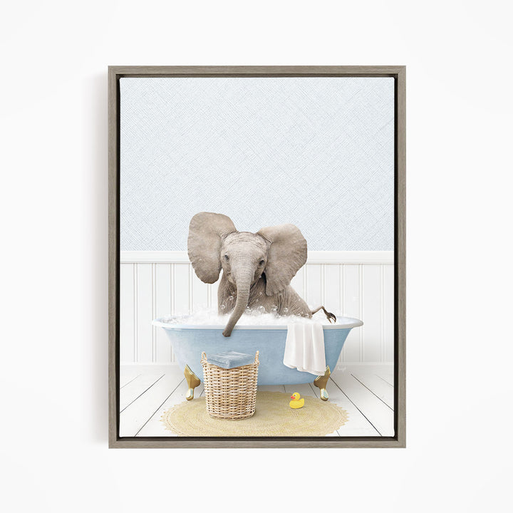 A gray elephant is sitting in a blue bathtub filled with water, surrounded by a yellow rubber duck and a basket.