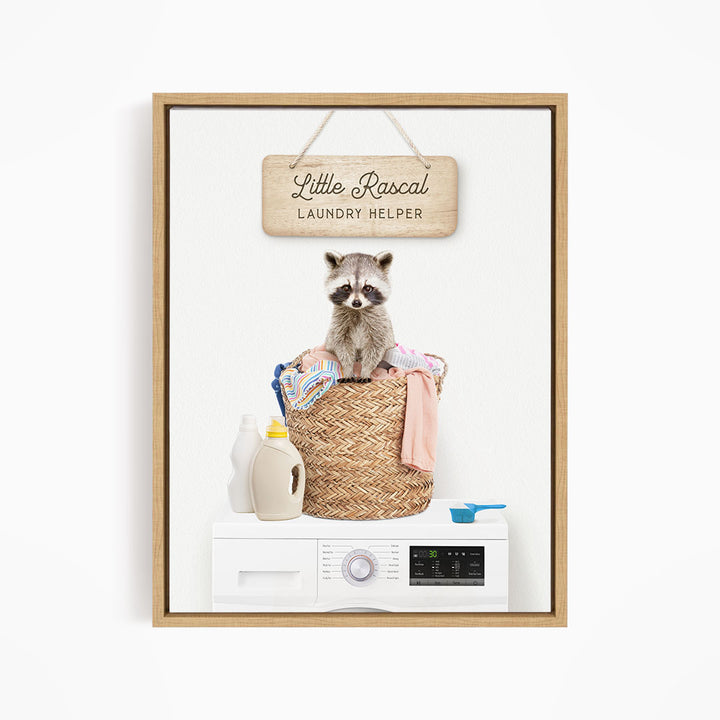A raccoon sitting in a woven laundry basket, with a sign that reads "Little Racal Laundry Helper" above it.