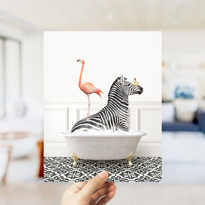 A hand holds up a framed image depicting a zebra sitting in a bathtub, with a pink flamingo standing on its back.