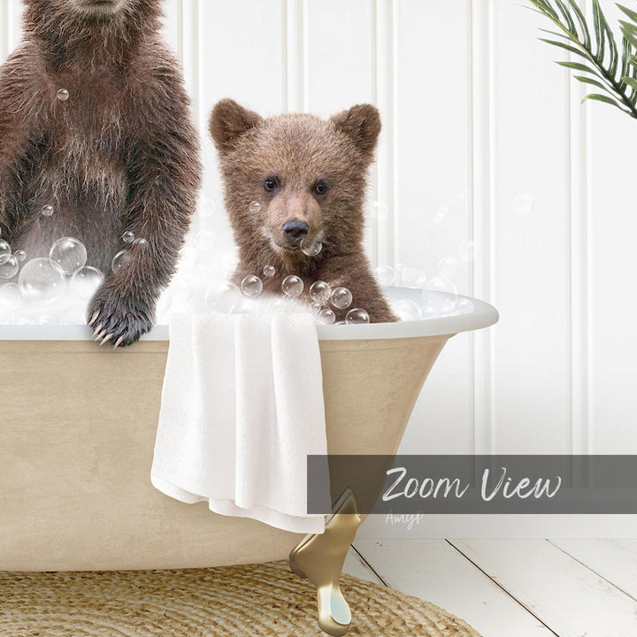 A baby bear sitting in a bathtub filled with bubbles, with a towel draped over the side of the tub.
