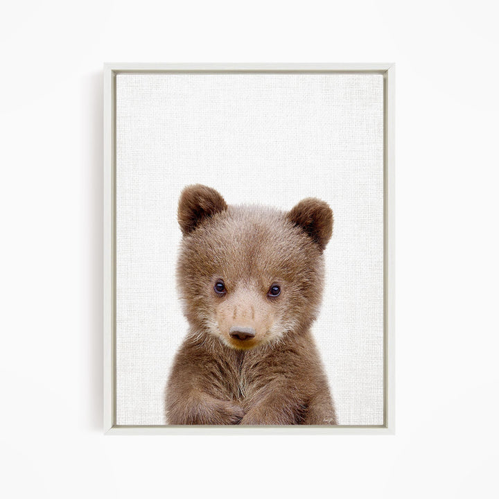 A cute brown bear cub with large eyes and a small nose is the focus of the image.