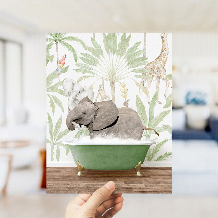 A hand holds up a framed print featuring an elephant bathing in a green bathtub, surrounded by tropical foliage and animals.