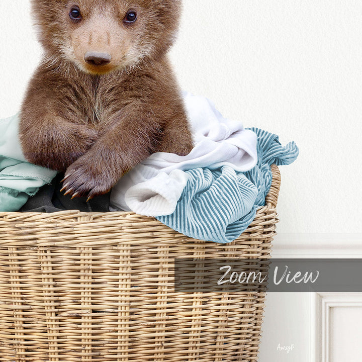 A brown bear sitting in a wicker basket filled with clothes.