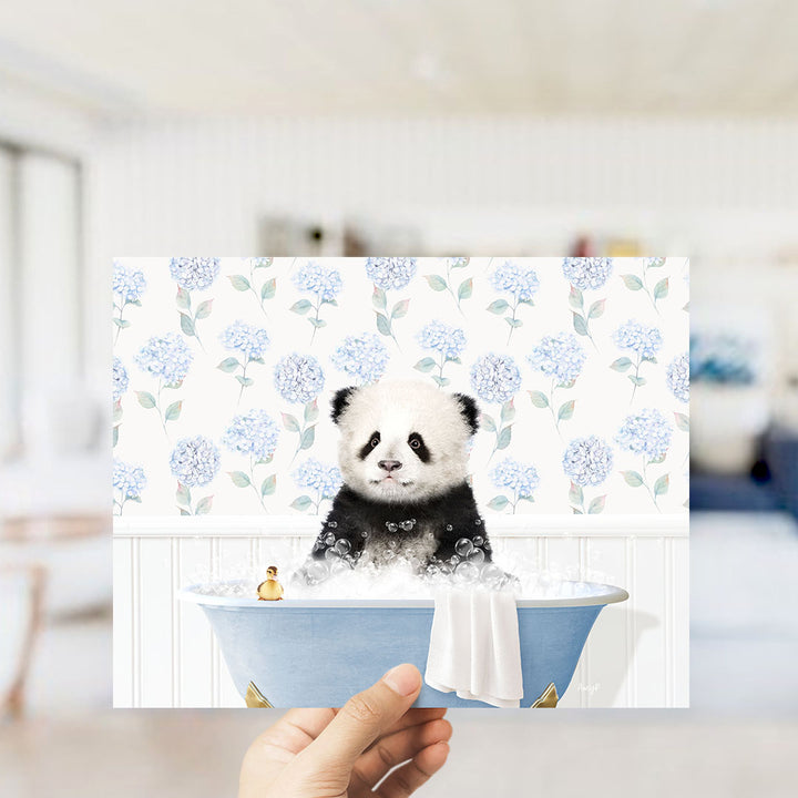A hand holding a framed print of a panda bear sitting in a bathtub filled with bubbles, surrounded by a floral pattern.