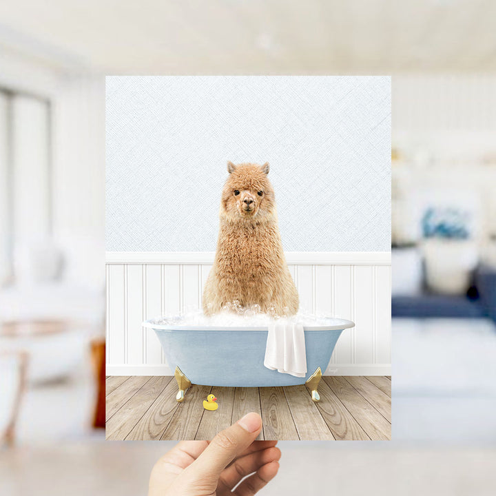 A fluffy brown alpaca sitting in a blue bathtub filled with bubbles, surrounded by a white bathtub, a yellow rubber duck, and a white towel.