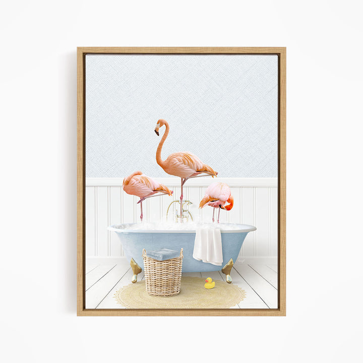 A framed image depicting three flamingos standing in a bathtub filled with water, surrounded by a basket of bath toys and a towel.