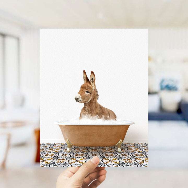 A donkey is sitting in a bathtub filled with bubbles, with a person's hand holding up the image.