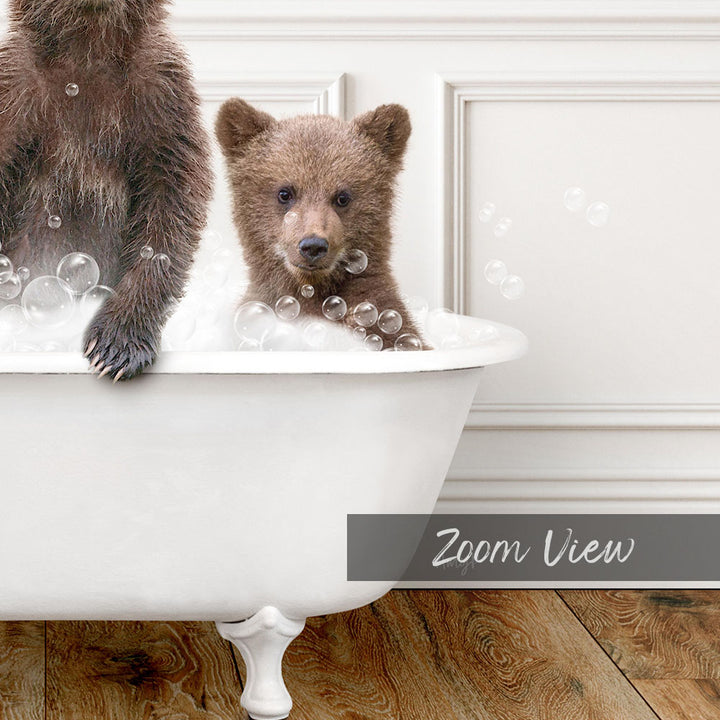 A baby bear sitting in a bathtub filled with bubbles, with a white wall and wooden floor in the background.