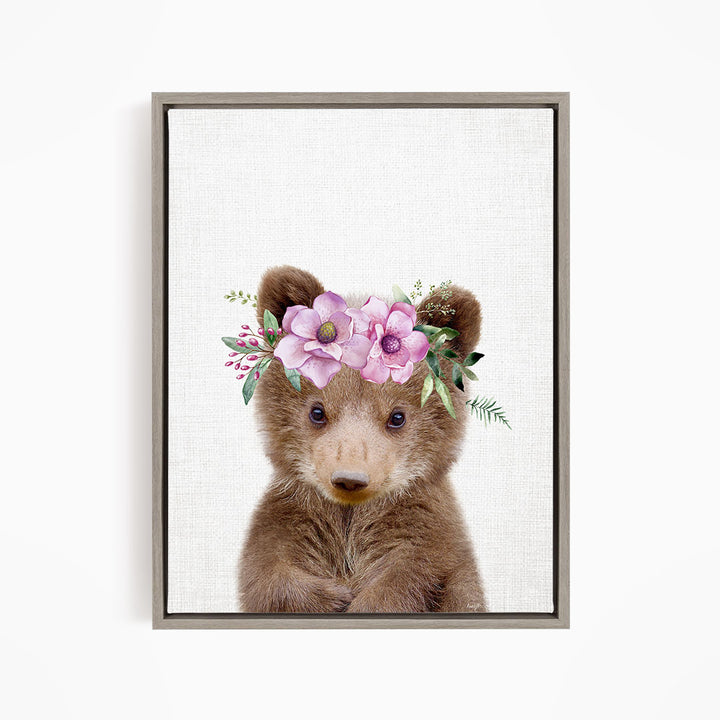 A cute brown bear wearing a floral crown of pink flowers and greenery.