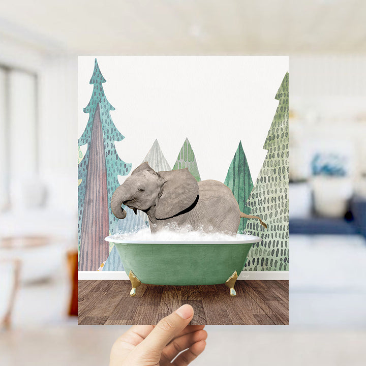 A hand holds up a framed image depicting a baby elephant sitting in a green bathtub, surrounded by a forest-themed background.