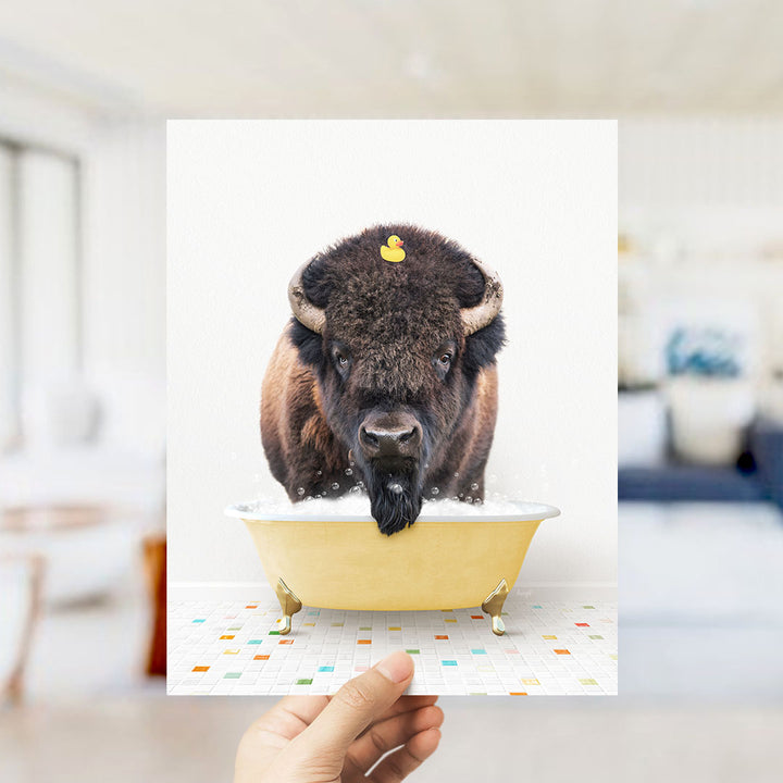 A buffalo with a yellow rubber duck in its mouth is sitting in a yellow bathtub, surrounded by colorful tiles on the floor.