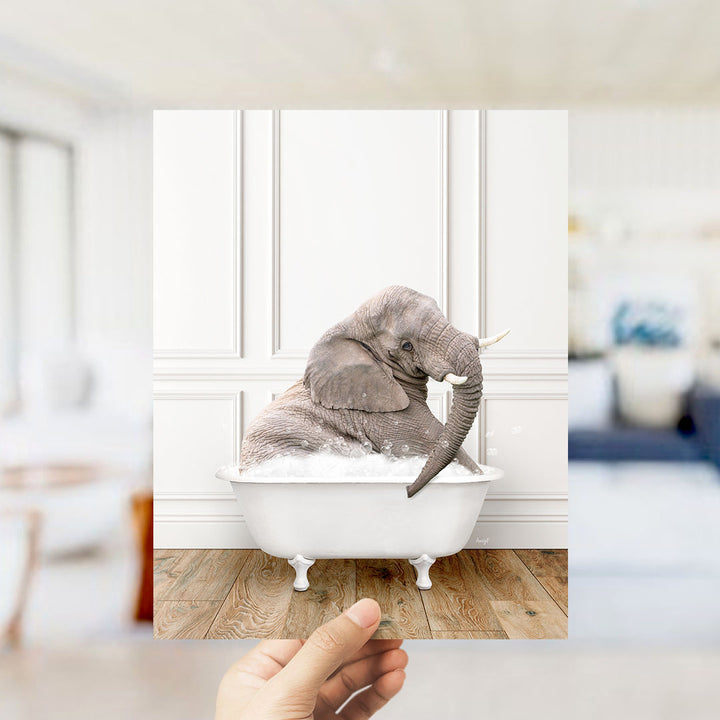 A gray elephant is sitting in a white bathtub filled with bubbles, surrounded by a blurred background.