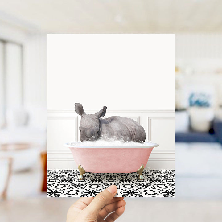 A rhinoceros is sitting in a pink bathtub filled with bubbles, creating a whimsical and playful scene.