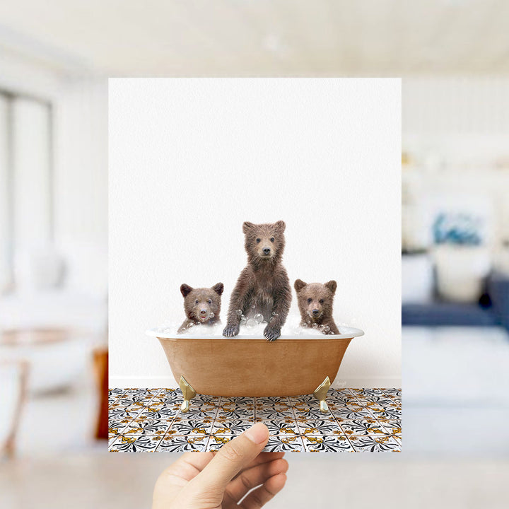 A hand holds up a framed image of three adorable brown bears sitting in a bathtub filled with water, creating a playful and whimsical scene.