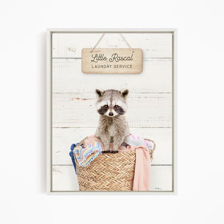 A raccoon sitting in a woven laundry basket, with a sign above that reads "Little Racal Laundry Service".