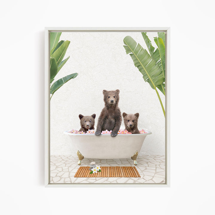 Three adorable brown bears sitting in a white bathtub filled with pink flowers, surrounded by green leaves.