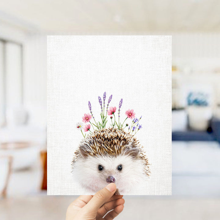 A hand is holding up a square print featuring a hedgehog with flowers on its head.
