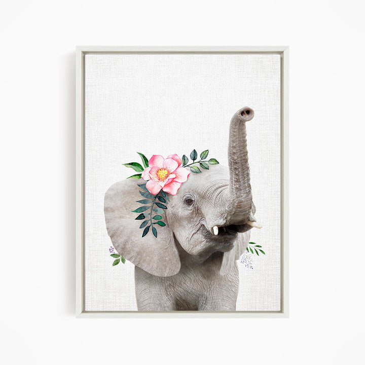 A gray elephant with a pink flower on its head and green leaves on its ears, standing against a white background.