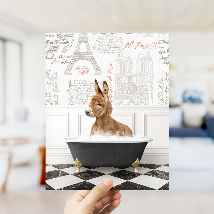 A hand holds up a collage of images featuring a donkey sitting in a bathtub, with the Eiffel Tower and Parisian architecture visible in the background.