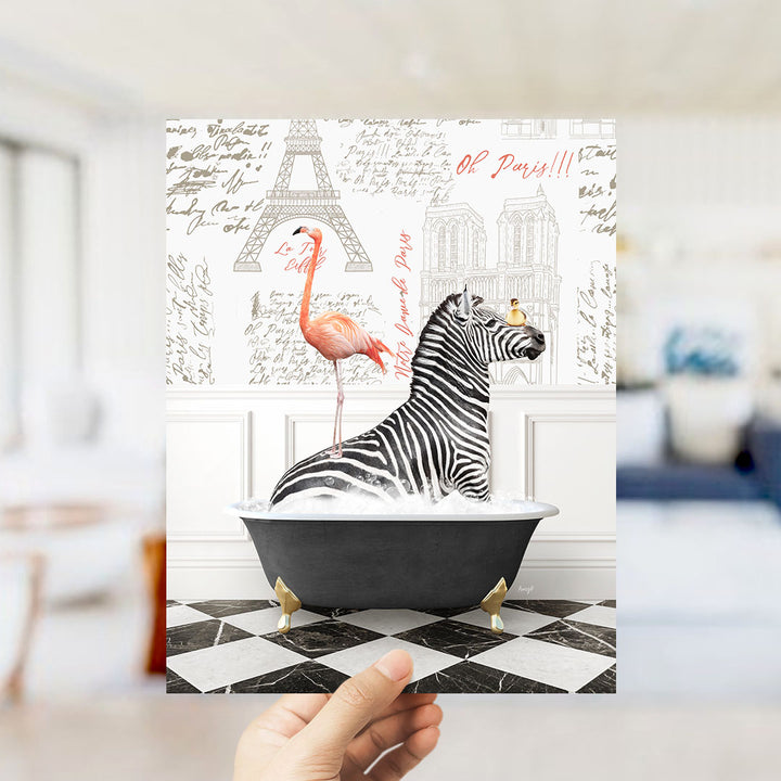 A hand holds up a print featuring a zebra sitting in a bathtub, with a pink flamingo standing on the edge of the tub. The background includes the Eiffel Tower and other Parisian landmarks.