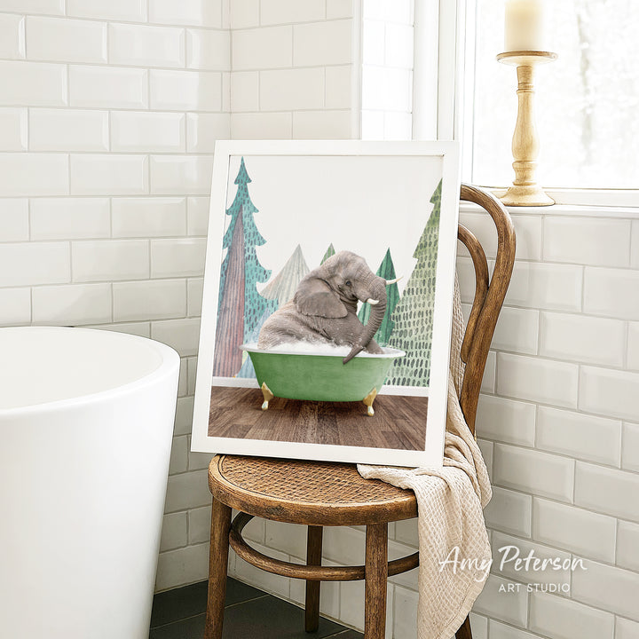 A framed painting of an elephant sitting in a green bathtub, surrounded by trees, is displayed on a wooden chair in a bathroom setting.
