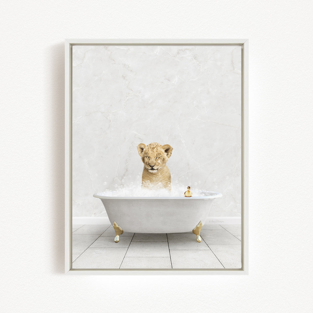 A young lion cub sitting in a white bathtub filled with bubbles, with a rubber duck floating in the water.