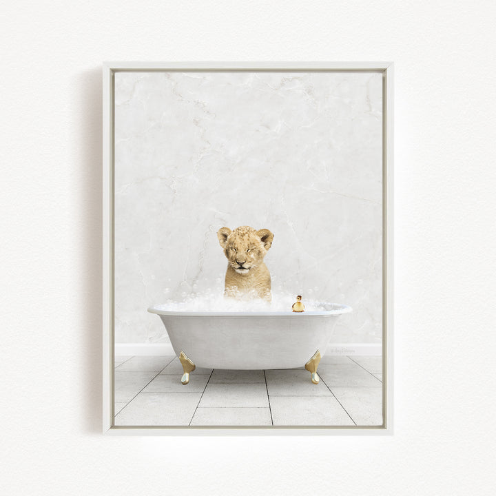A young lion cub sitting in a white bathtub filled with bubbles, with a rubber duck floating in the water.