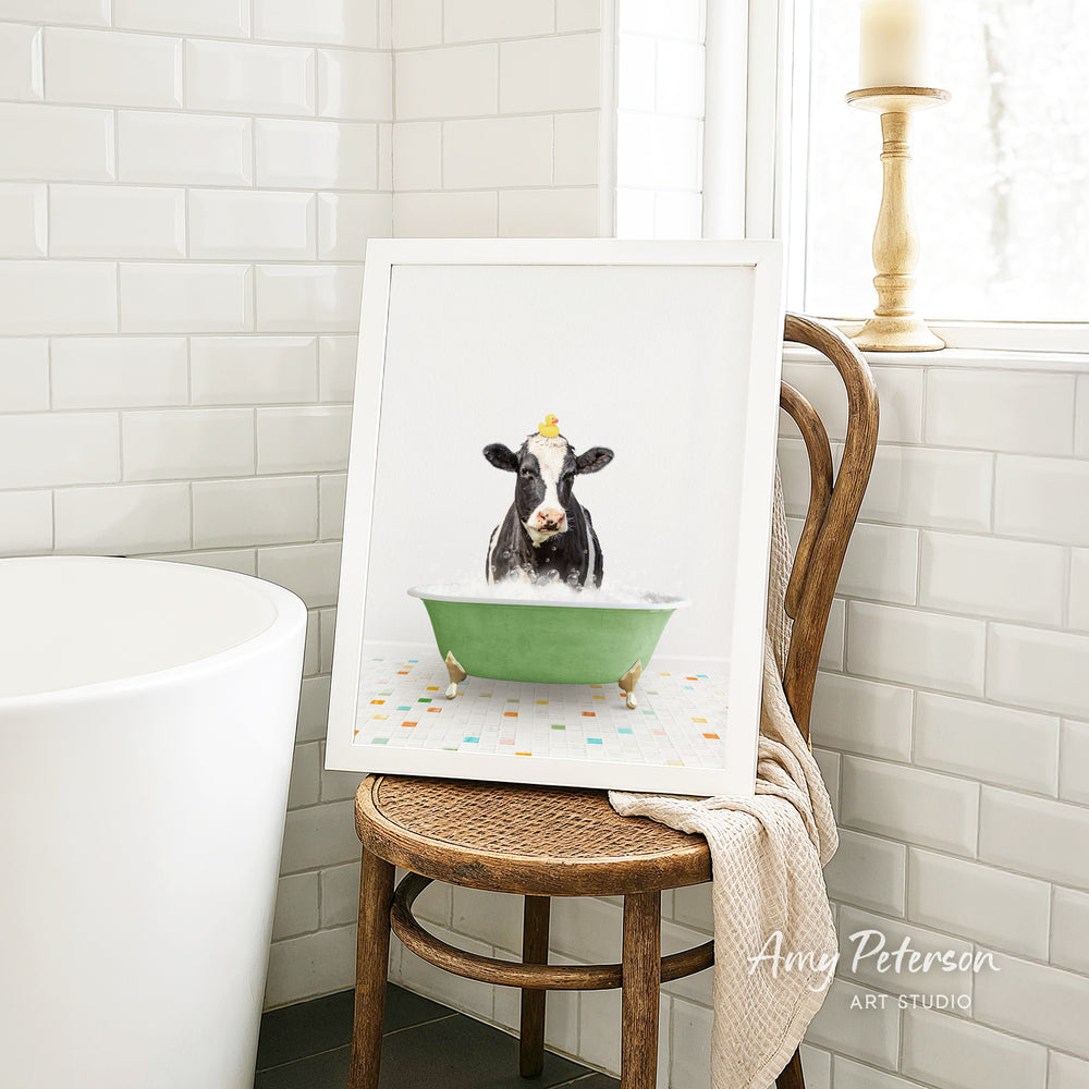 A framed image of a cow sitting in a green bathtub, surrounded by colorful tiles, is displayed on a wooden chair in a bathroom setting.