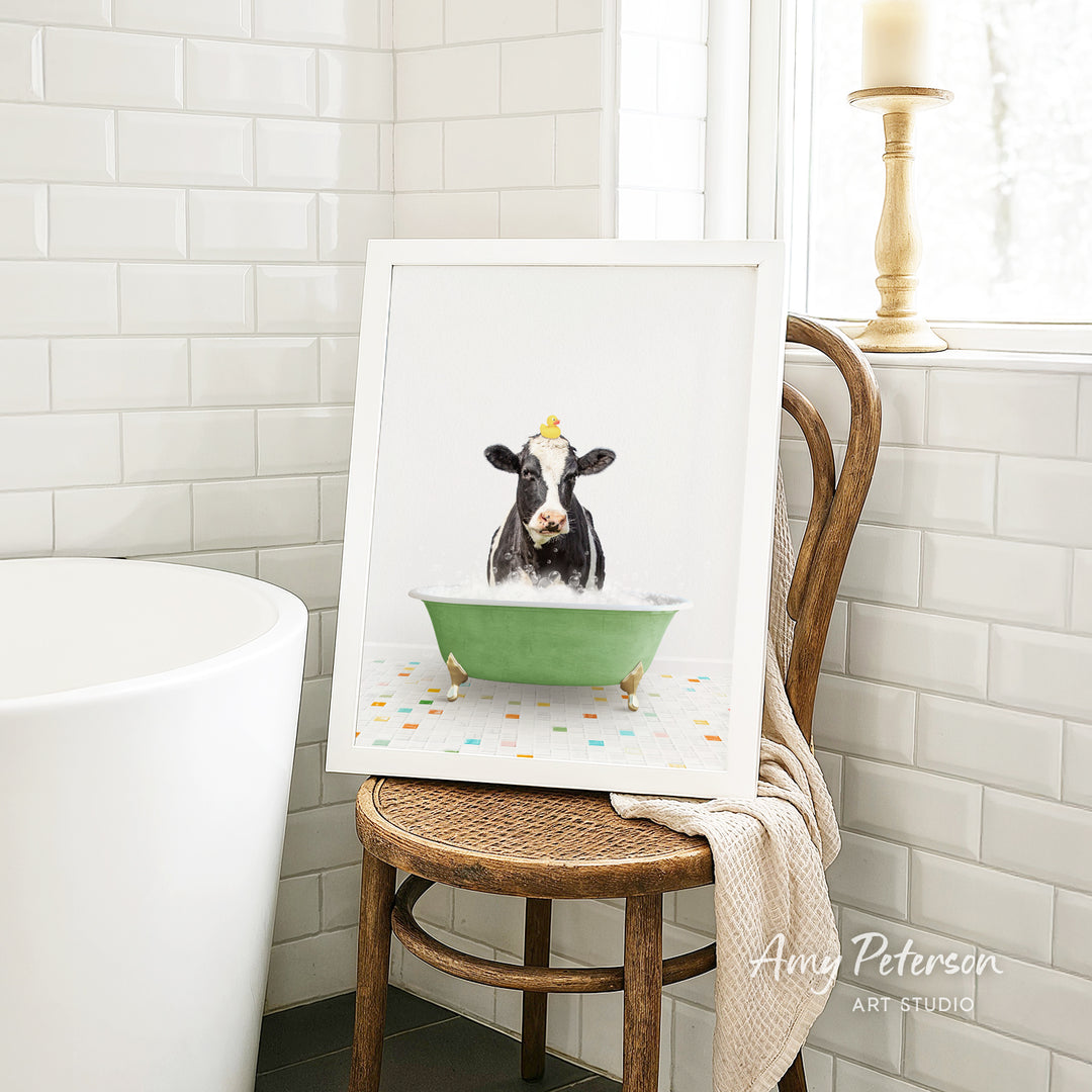A framed image of a cow sitting in a green bathtub, surrounded by colorful tiles, is displayed on a wooden chair in a bathroom setting.