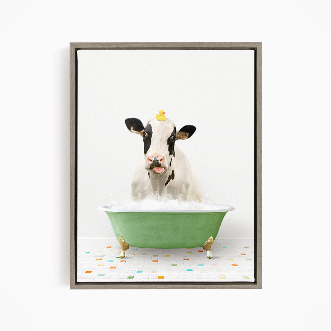 A black and white cow is sitting in a green bathtub filled with bubbles, with a yellow rubber duck perched on its head.