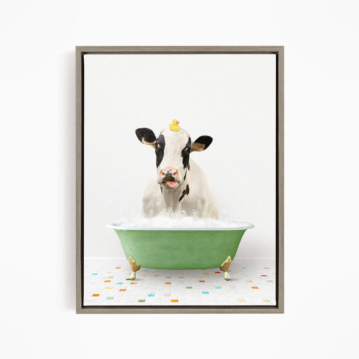 A black and white cow is sitting in a green bathtub filled with bubbles, with a yellow rubber duck perched on its head.
