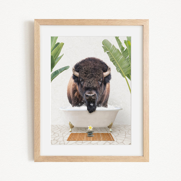 A buffalo is sitting in a bathtub filled with water, surrounded by tropical plants and a wooden mat on the floor.