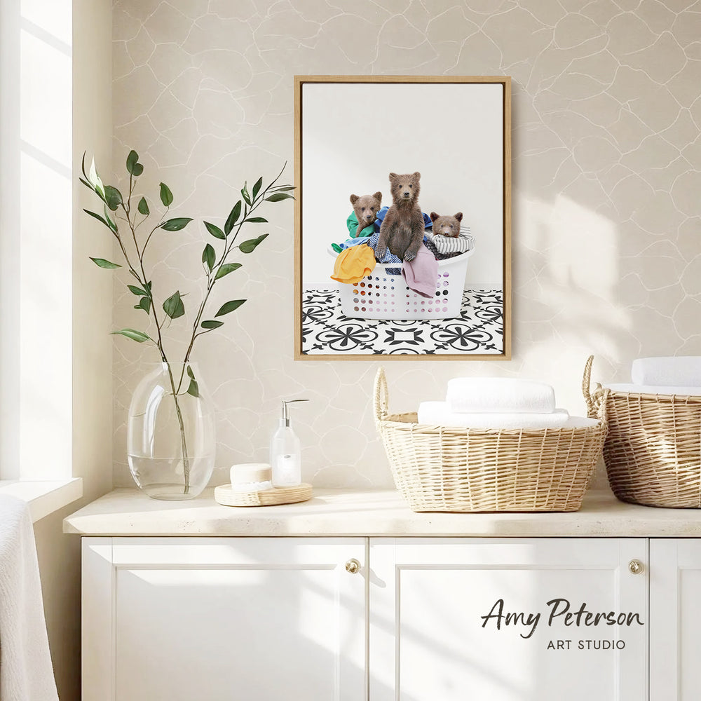 a framed photograph of three bears sitting in a laundry basket, placed on a wall above a white cabinet.