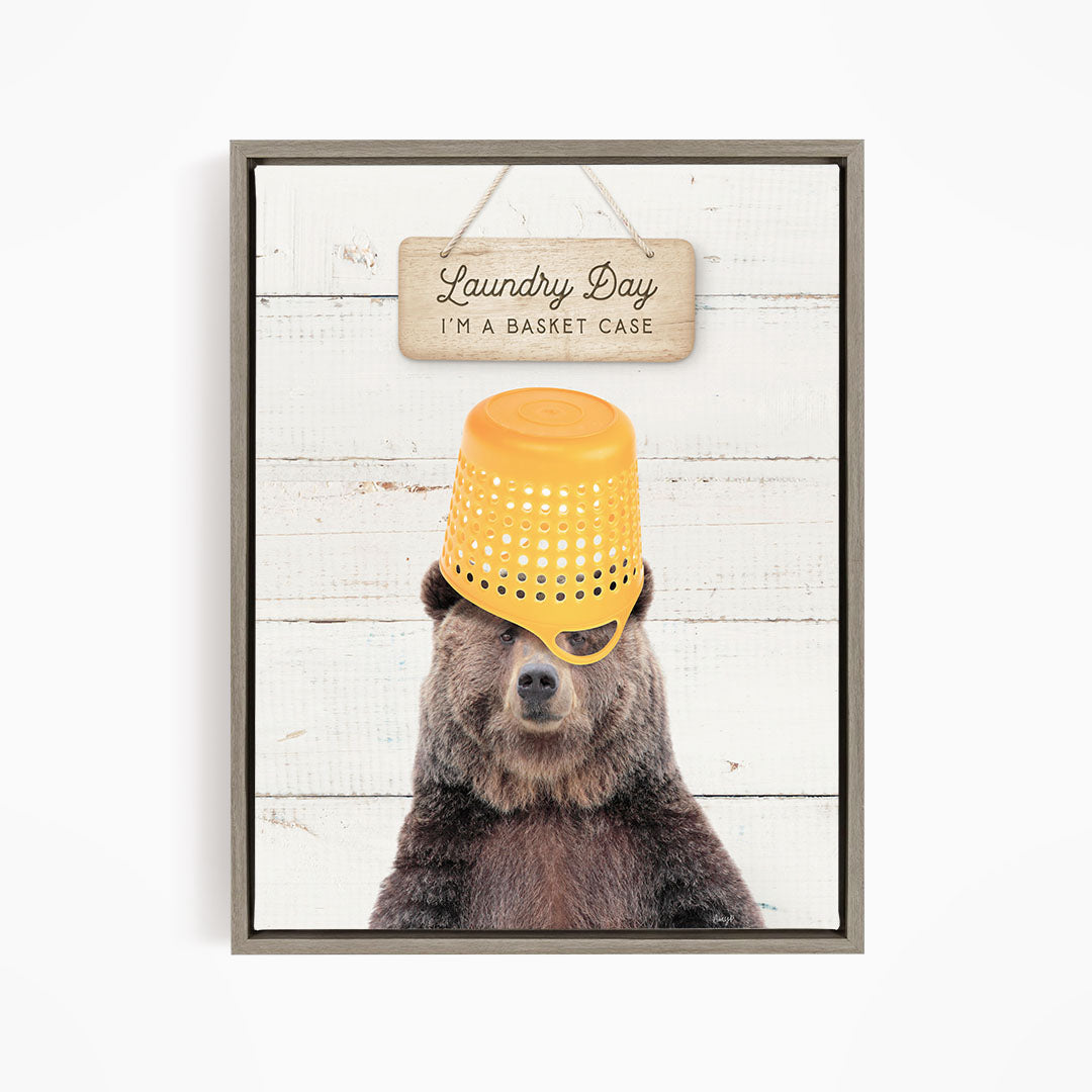 A framed image of a bear wearing a yellow basket on its head, with a sign above that says "Laundry Day I'm a basket case".