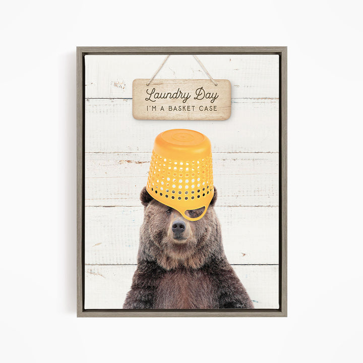 A framed image of a bear wearing a yellow basket on its head, with a sign above that says "Laundry Day I'm a basket case".