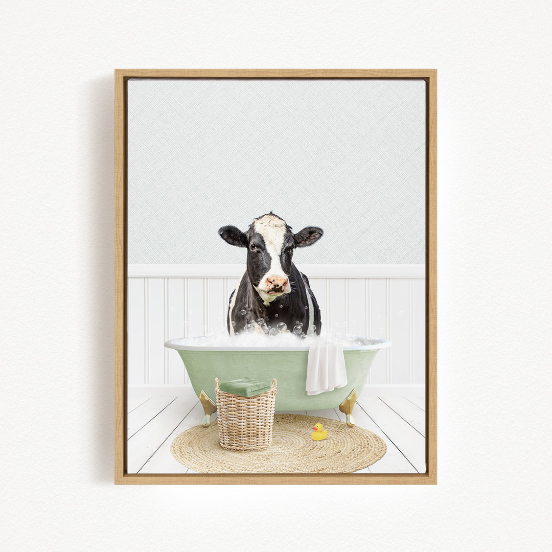 A black and white cow is sitting in a green bathtub filled with water, surrounded by a basket of rubber ducks and a towel.