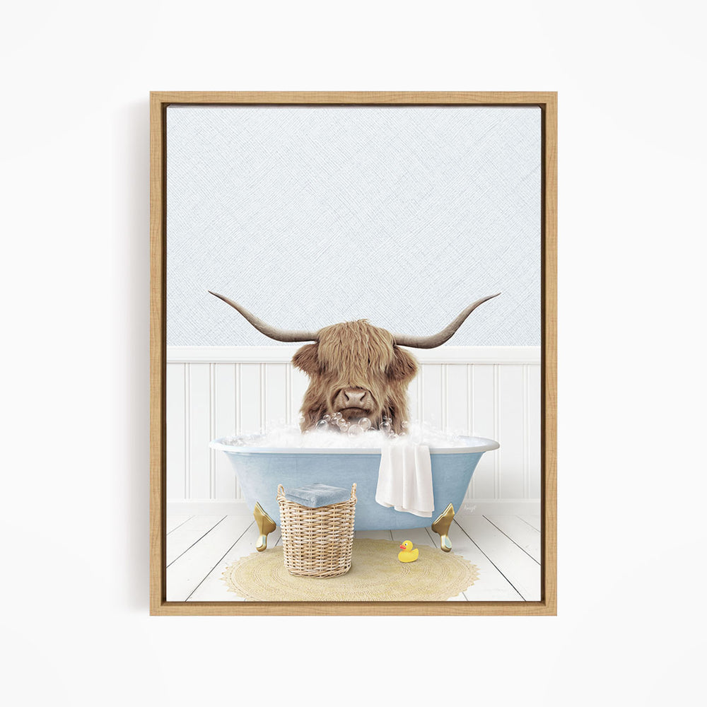 A brown cow with long horns is sitting in a blue bathtub, surrounded by a basket of rubber ducks and a towel.