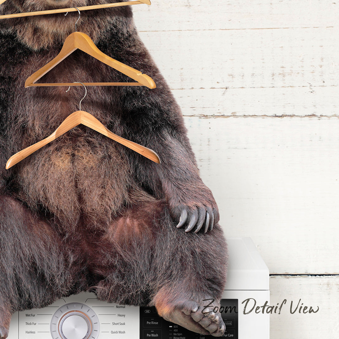 A bear sitting on a washing machine with clothes hangers hanging from its back.