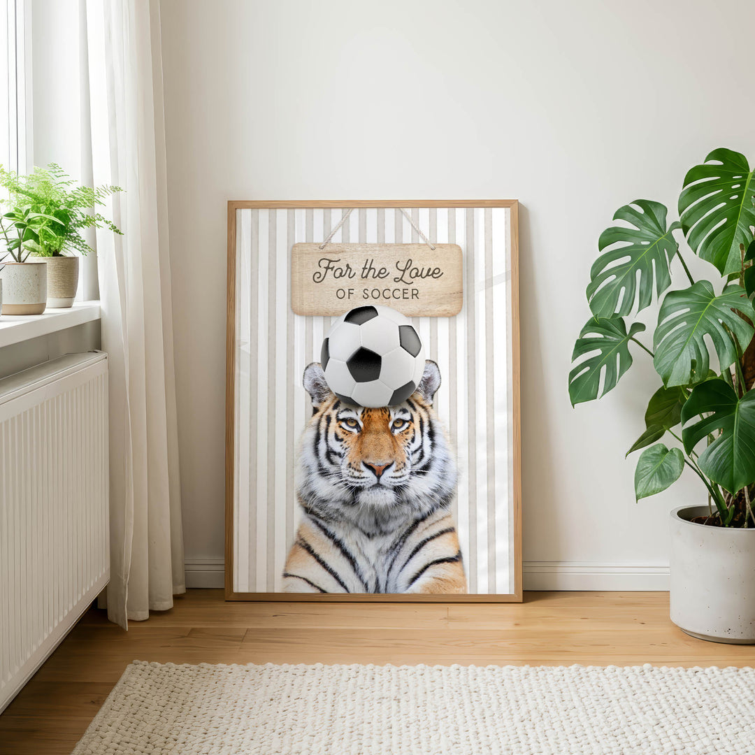 A framed poster of a tiger with a soccer ball on its head, placed on a wall in a room with a rug and potted plants.