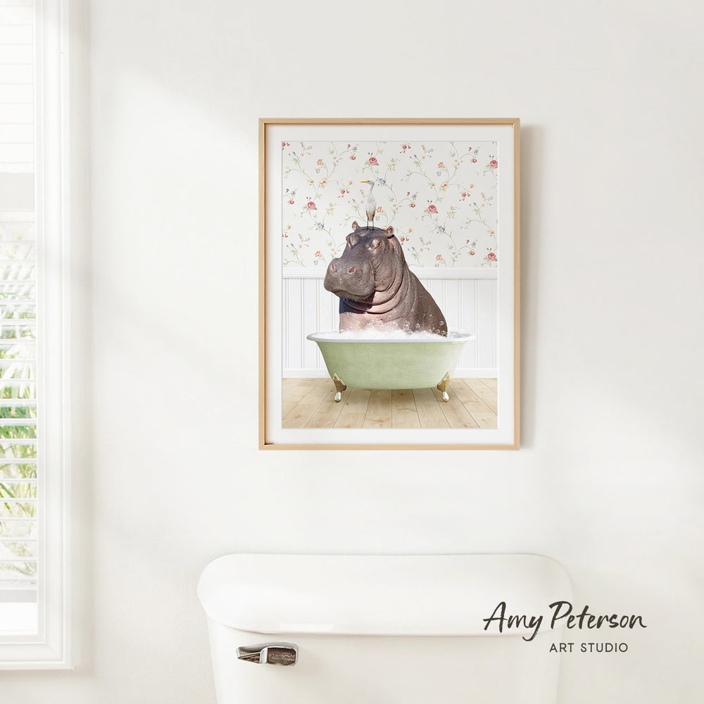 A framed image of a hippopotamus sitting in a bathtub, with a floral pattern on the wall behind it.