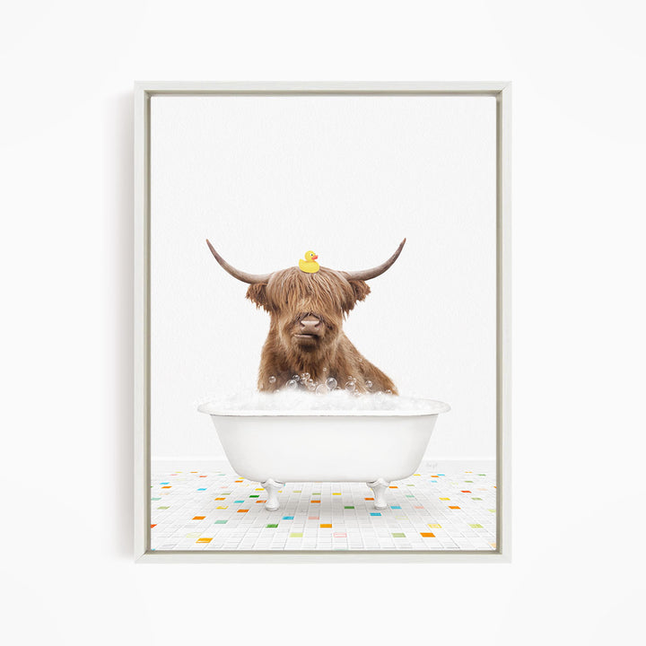 A brown cow with long horns is sitting in a white bathtub filled with bubbles, with a rubber duck perched on its head.