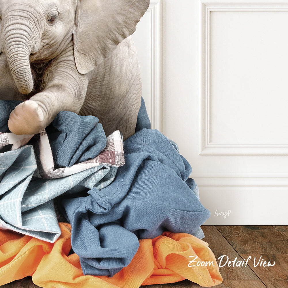 A baby elephant sitting on a pile of clothes, with a white door and wooden floor in the background.