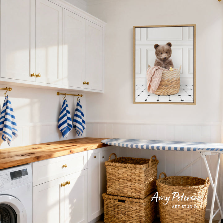 A cozy laundry room with white cabinets, a wooden countertop, and a framed image of a cute bear sitting in a basket.