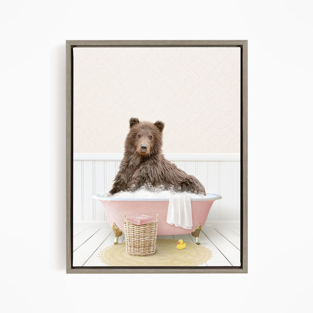 A brown bear sitting in a pink bathtub filled with bubbles, surrounded by a yellow rubber duck and a basket.