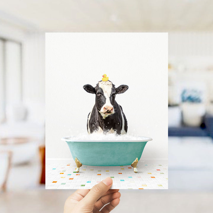 A black and white cow is sitting in a green bathtub filled with bubbles, with a yellow rubber duck perched on its head.
