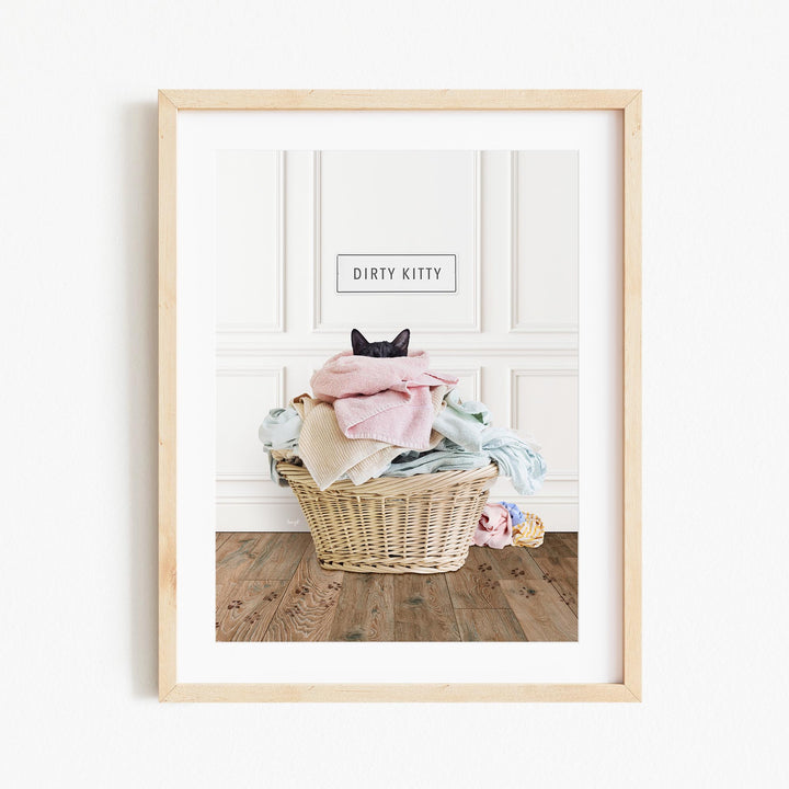 A framed image of a cat sitting in a basket filled with clothes, with the text "Dirty Kitty" displayed above the cat.