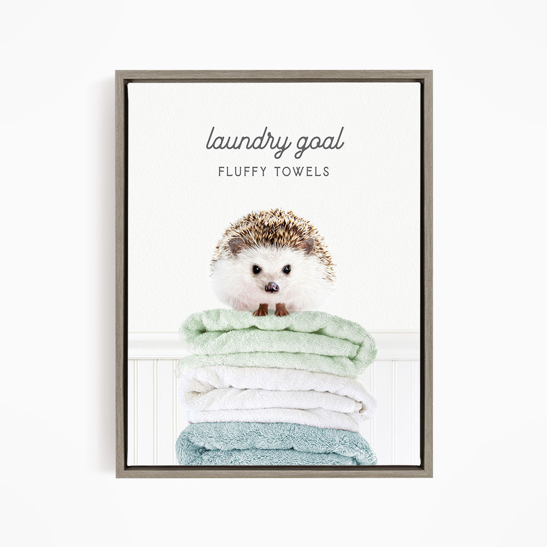 A framed image of a hedgehog sitting atop a stack of fluffy towels, with the text "laundry goal FLUFFY TOWELS" written above it.