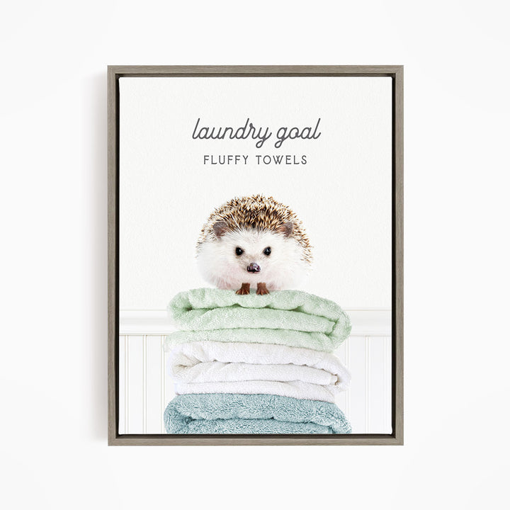 A framed image of a hedgehog sitting atop a stack of fluffy towels, with the text "laundry goal FLUFFY TOWELS" written above it.