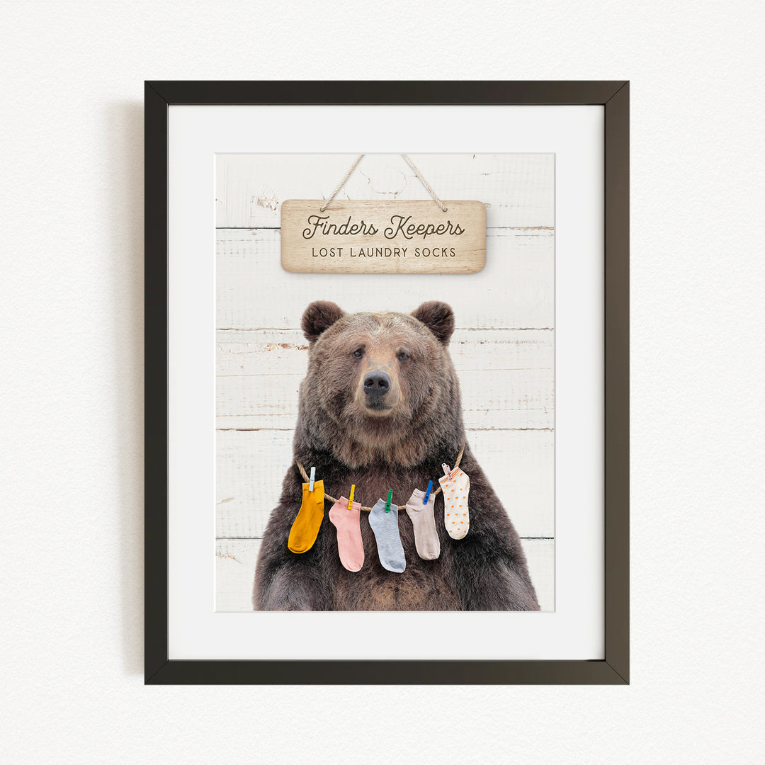 A framed image of a brown bear wearing colorful socks hanging on a clothesline.
